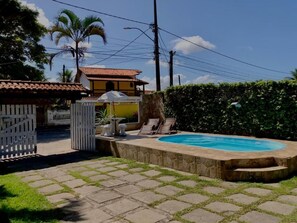 A swimming pool with a stone edge, a white fence, and a yellow building in the background. - Pousada do Suiço (Saquarema)