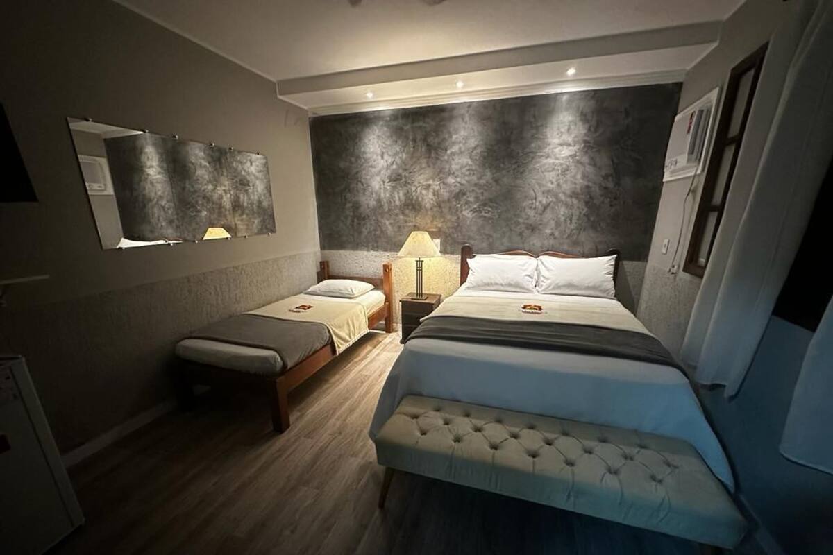 A bedroom with two beds, a bedside table with a lamp, and a large mirror on the wall.