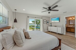 Quarto com cama grande, ventilador de teto, vista para o exterior, banheiro com toucador e área de jantar.