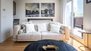 Una sala de estar moderna con un sofá beige, una mesa redonda de centro y dos grandes cuadros con paisajes urbanos en la pared.