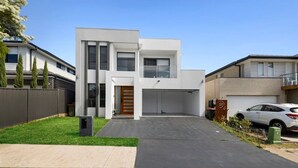 Une maison moderne à deux étages, dotée d’un garage, d’une pelouse bien entretenue et d’une voiture garée.