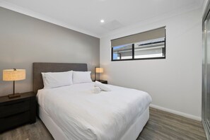 A hotel room with a large bed, two bedside lamps, a window with blinds, and a view of the sky.