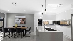 Une cuisine moderne avec des meubles blancs, un îlot central et un coin repas comprenant une table et des chaises.