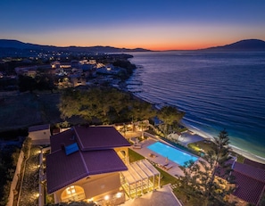 Una propiedad costera con piscina, un patio cubierto y vistas al mar al atardecer.
