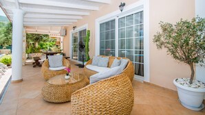 A covered patio area with wicker furniture, a potted plant, and a view of the garden. - Zante Sun I - Getaway Villa! (Zakynthos)