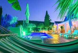 Relax by the pool surrounded by lush greenery and palm trees, with lounge chairs and a hammock for ultimate leisure.