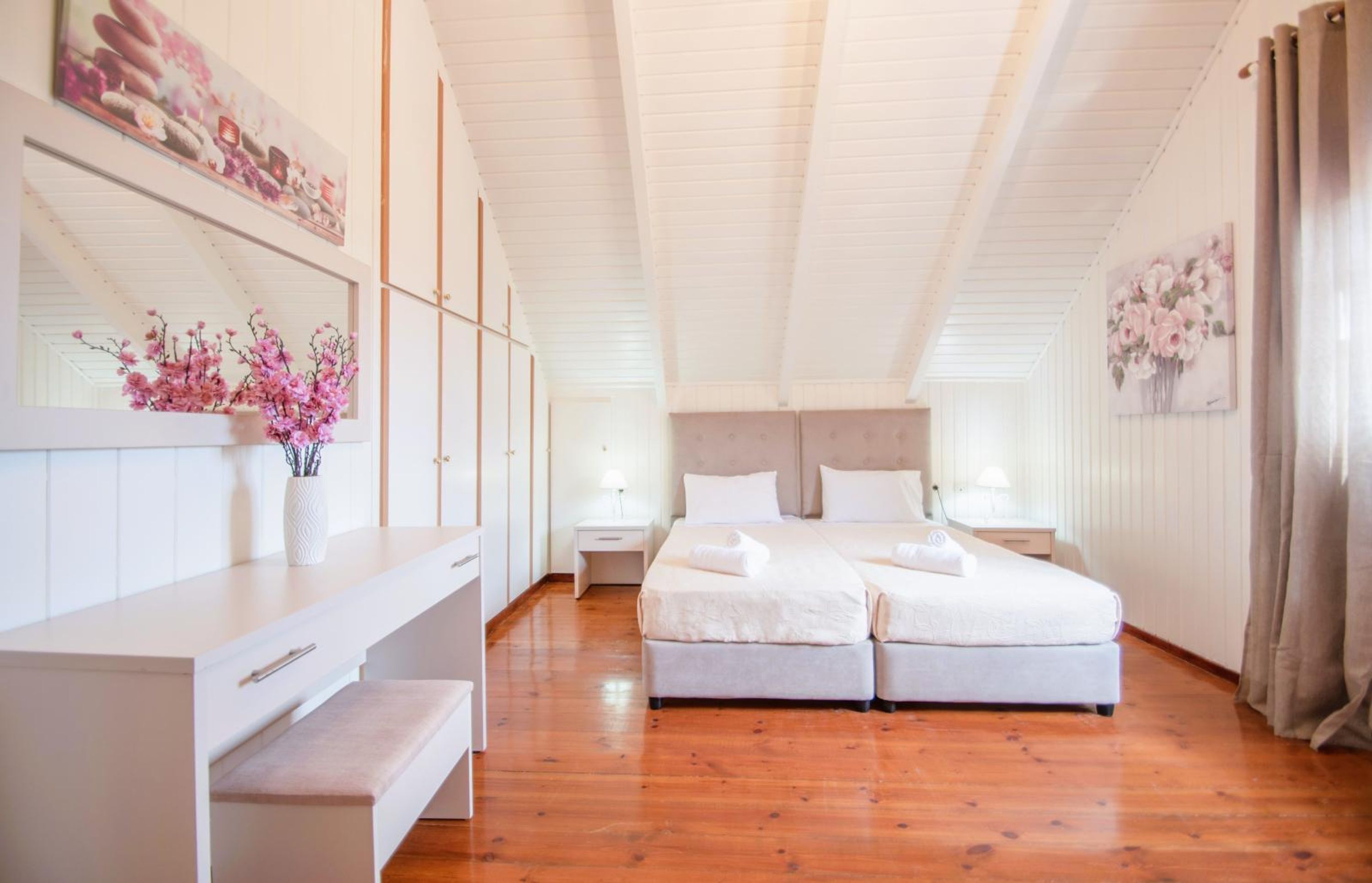 Une chambre avec deux lits, un plancher en bois, une commode blanche et une grande fenêtre avec des rideaux.