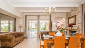 Un salon spacieux comprenant un canapé, une table à manger et des chaises, un lustre et une cheminée agrémentée d’un miroir.