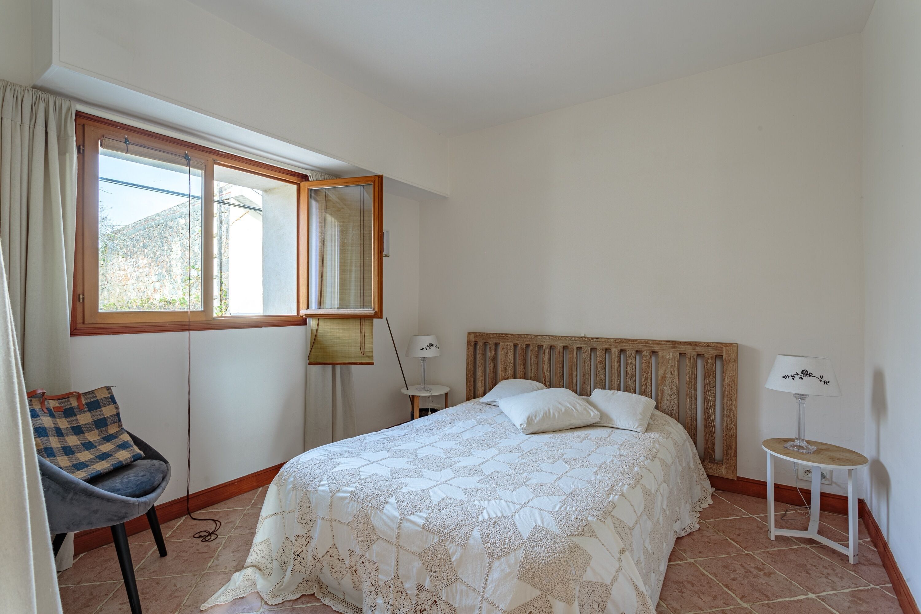 A bedroom with a bed, a chair, a nightstand, a lamp, and a window.
