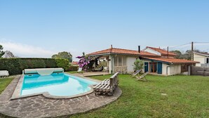 Un patio trasero con piscina, un porche cubierto y una casa con techo de tejas.