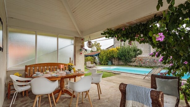 Un patio cubierto con mesa y sillas de madera, un sofá de mimbre y vista a una piscina.