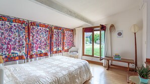 Un dormitorio con una cama grande, un banco de madera, una planta en maceta y vistas al exterior.