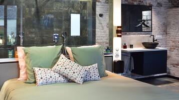 Une chambre moderne avec un grand lit, une literie verte, un coussin orné de motifs en forme d’étoiles, un lavabo noir et un miroir au-dessus.