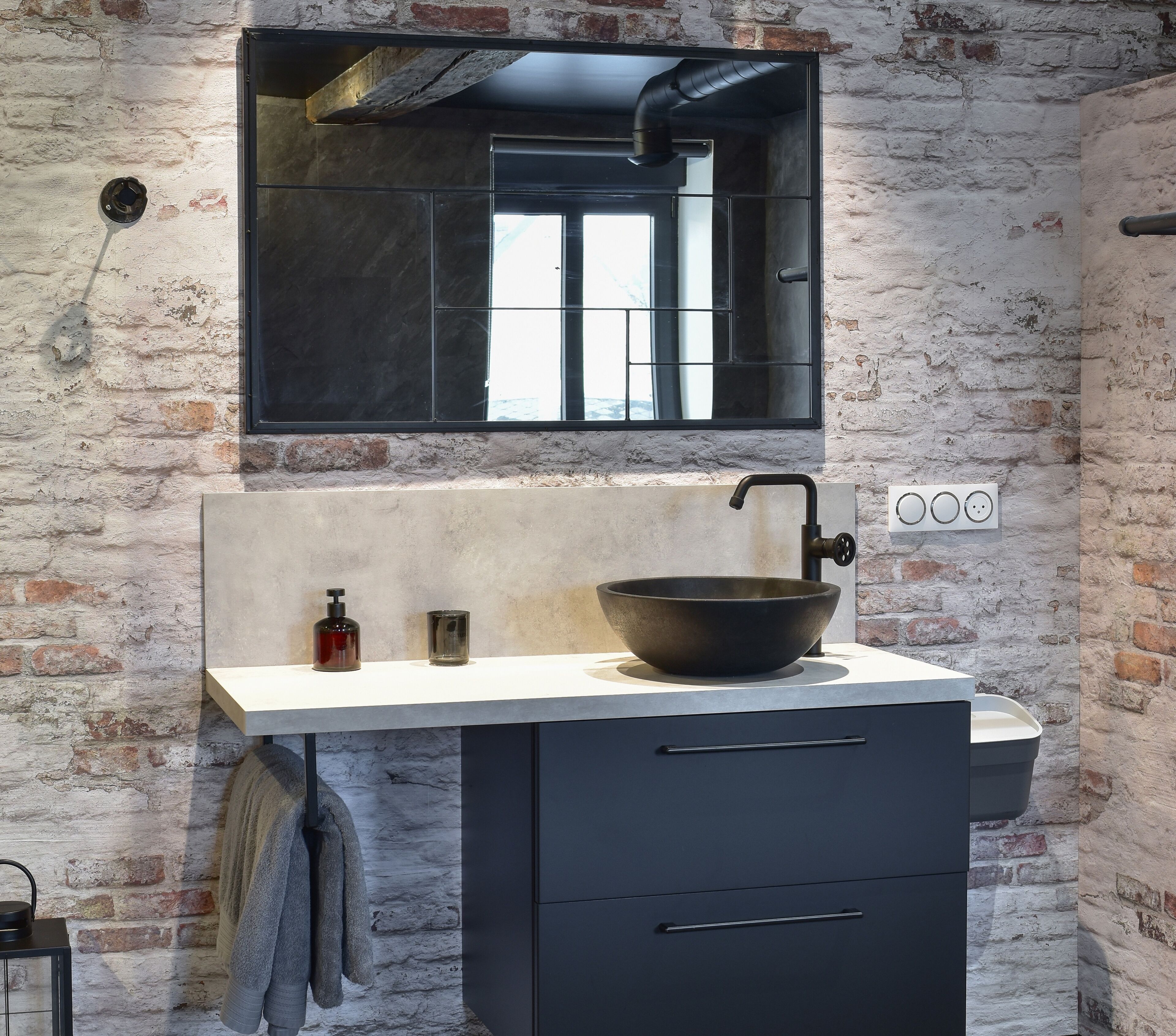 A modern bathroom with a large black basin, a mirror above the sink, and a brick wall.