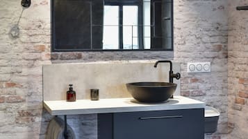 A modern bathroom with a large black basin, a mirror above the sink, and a brick wall.