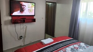 Habitación de hotel con cama, televisión montada en la pared, espejo y ventana con cortinas.
