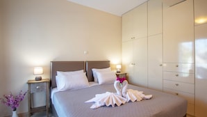 A neatly made bed with white linens and two pillows, a bedside table with a lamp, a vase with flowers, and a wardrobe with multiple doors. - Zante Sun II - Getaway Villa! (Zakynthos)