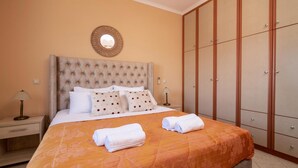 A neatly made bed with a patterned bedspread and pillows, a bedside lamp, and a wardrobe with multiple doors. - Matina's Family House With Your Private Jacuzzi! (Zakynthos)
