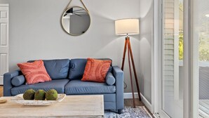 Een kamer met een blauwe bank, een ronde spiegel, een vloerlamp en een raam met jaloezieën.