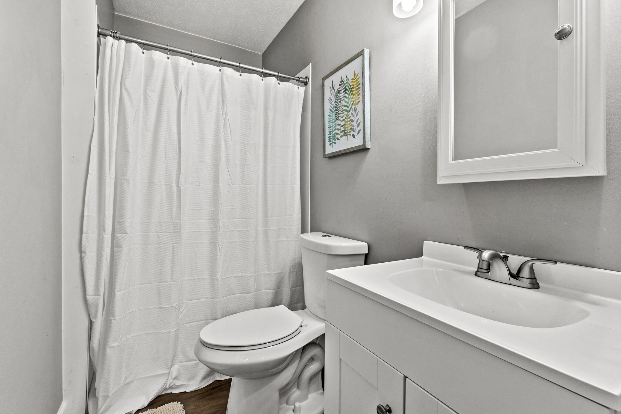 Un baño con inodoro y lavamanos blancos, y cortina de ducha.