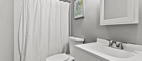 Un baño con inodoro y lavamanos blancos, y cortina de ducha.