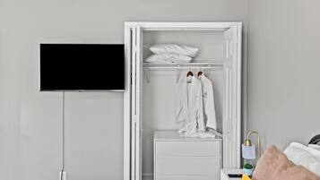 A bedroom with a white wardrobe, a bedside table with a lamp, and a bed with a pink pillow.