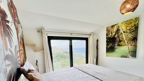 A bedroom with a large bed, a view of the landscape, and a painting on the wall. - Mar a Vista by Your Madeira Rentals (Ponta do Sol)
