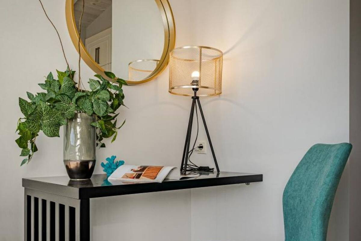 A modern room with a black console table, a teal chair, a potted plant, a round mirror, and a floor lamp.