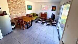 En kompakt opholdsstue med spiseplads, sofa, fjernsyn og et tekøkken med køleskab.