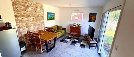 A compact living space with a dining area, a sofa, a TV, and a kitchen area with a refrigerator.