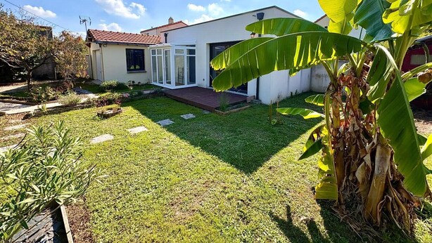 Et moderne hus med en velplejet græsplæne, en terrasse og et stort banantræ.