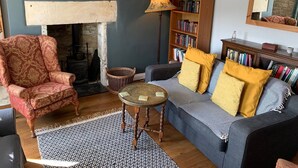 A cozy living room with a fireplace, a bookshelf, a patterned rug, and a comfortable sofa. - Traditional Cotswold cottage with stunning views and walking (Stroud)