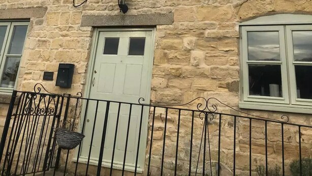 A stone building with a white door, two windows, and a small balcony with a metal railing. - Traditional Cotswold cottage with stunning views and walking (Stroud)