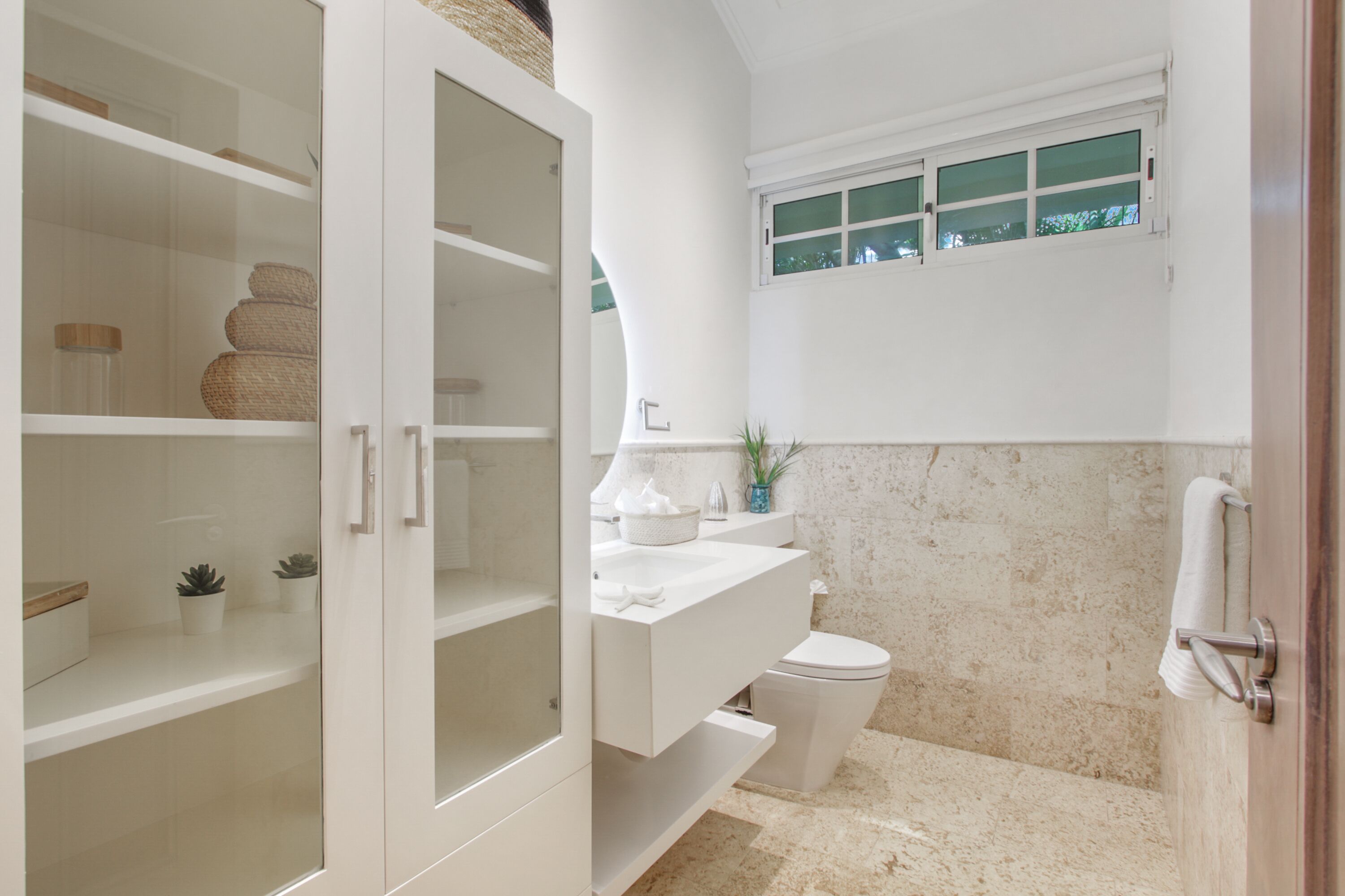A bathroom with a white vanity, a toilet, and a glass cabinet with baskets.