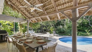 An outdoor dining area with a thatched roof, a pool, and lounge chairs. - 5BR Villa with Pool&Beach in Punta Cana (Punta Cana)