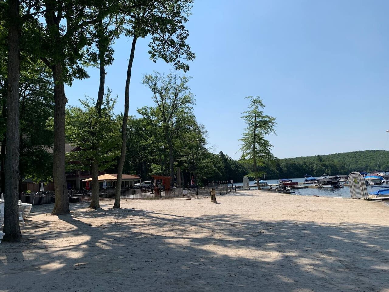 Une plage de sable bordée d’arbres, avec une petite construction et des bateaux en arrière-plan.