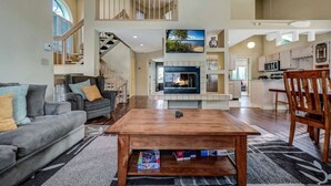 A spacious living room with a fireplace, a dining area with a wooden table, and a kitchen in the background. - Walk 2 Ski: Groups, Kids, Spacious & Well-Stocked (Lake Harmony)
