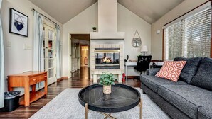 A spacious living room with a fireplace, a sofa, a coffee table, and a dining area visible in the background. - Walk 2 Ski: Groups, Kids, Spacious & Well-Stocked (Lake Harmony)