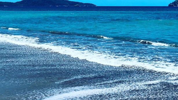 Una playa con aguas azules cristalinas y colinas a lo lejos.