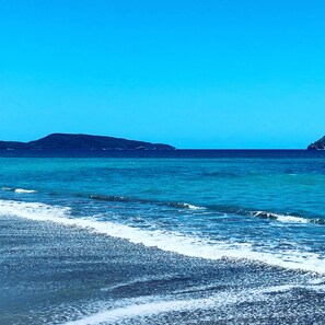 Een strand met helderblauw water en heuvels in de verte.
