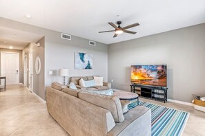 A living room with a beige sofa, a flat-screen TV, a ceiling fan, and a painting on the wall.