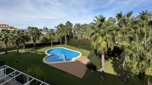 A swimming pool surrounded by palm trees and a well-maintained lawn. - Apartamento en la Playa las Marinas en Denia (VC)