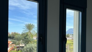 A room with two windows, one of which offers a view of a residential area with palm trees and a parked car. - Apartamento en la Playa las Marinas en Denia (VC)