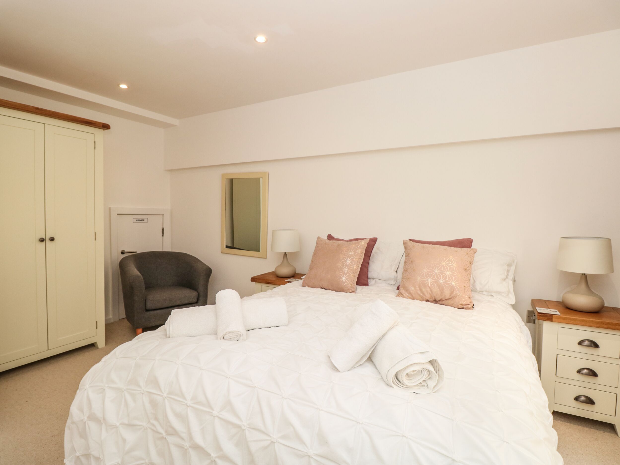 A hotel room with a bed, a chair, a nightstand, a lamp, and a wardrobe.