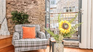 Une pièce chaleureuse avec un fauteuil à carreaux, un vase contenant un tournesol et des bougies posées sur une table en bois.