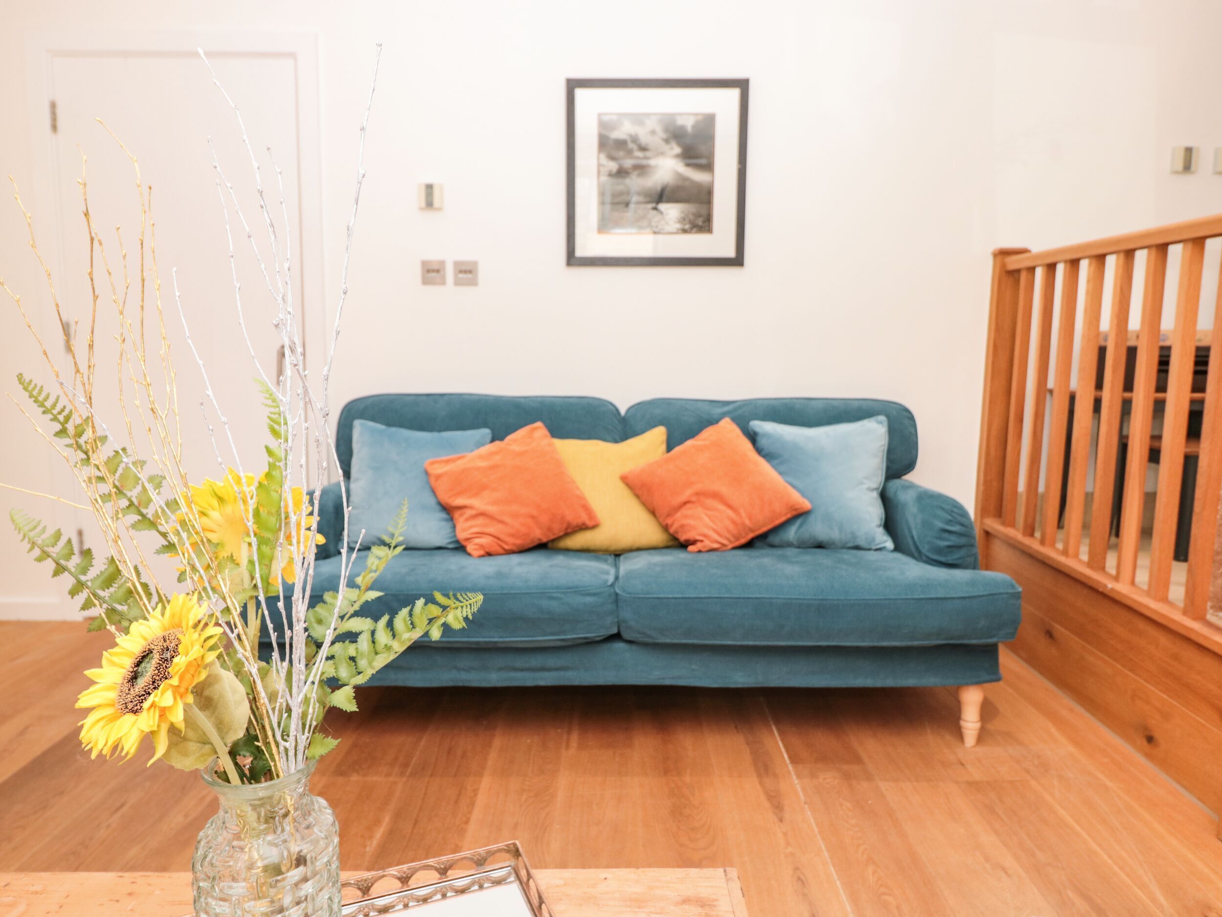 A living room with a blue sofa, a wooden floor, and a framed picture on the wall.