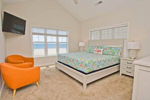 A bedroom with a bed, two chairs, a TV, and a window with a view.