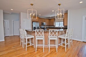 A modern kitchen with a central island, white bar stools, and pendant lighting.