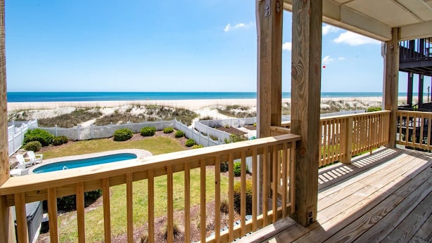 Terraza de madera con vista a una playa y una piscina.