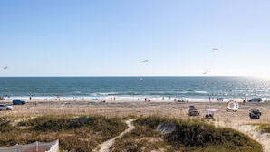 Una playa con un sendero arenoso que lleva al agua, un puesto de salvavidas y algunos vehículos estacionados.